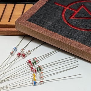 May include: A collection of electronic components, including diodes with colored bands, and a wooden coaster with a red symbol etched into it. The diodes have clear glass bodies with colored bands of red, green, yellow, and blue. The coaster has a dark gray surface.