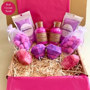 May include: A pink gift box filled with bath products, including bath salts, bath bombs, and bath fizzies. The box is decorated with pink tissue paper and straw. The bath products are labelled with the names "Diamond Dust" and "Rose Quartz".