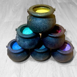May include: A set of seven black cauldron-shaped containers with colorful glitter inside. The cauldrons are stacked in a pyramid shape.