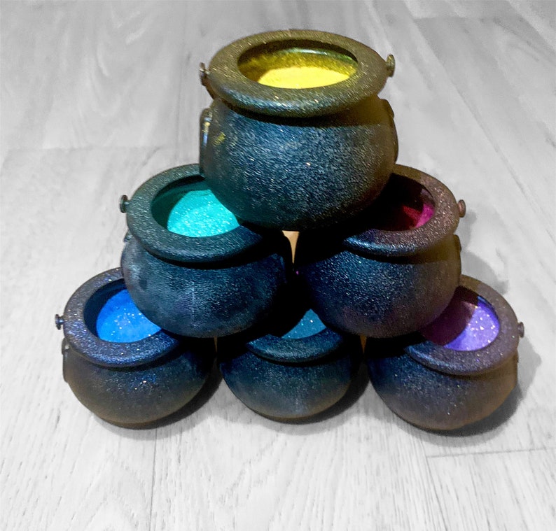 May include: A set of seven black cauldron-shaped containers with colorful glitter inside. The cauldrons are stacked in a pyramid shape.