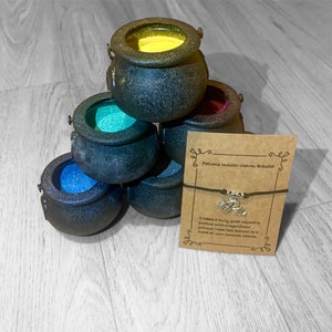 May include: A black string bracelet with a silver charm shaped like a cauldron. The bracelet is displayed on a brown card with the text "Potions master charm bracelet" and a description about the charm.