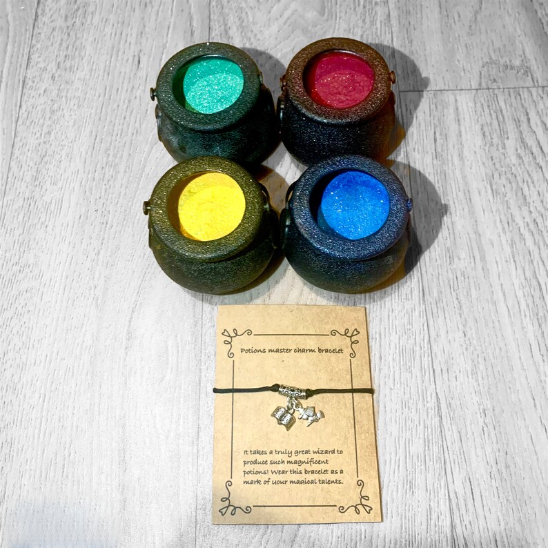 May include: A brown card with the text "Potions master charm bracelet" and "It takes a truly great wizard to produce such magnificent potions! Wear this bracelet as a mark of your magical talents."  A black string bracelet with a silver charm of a cauldron with a heart on top.