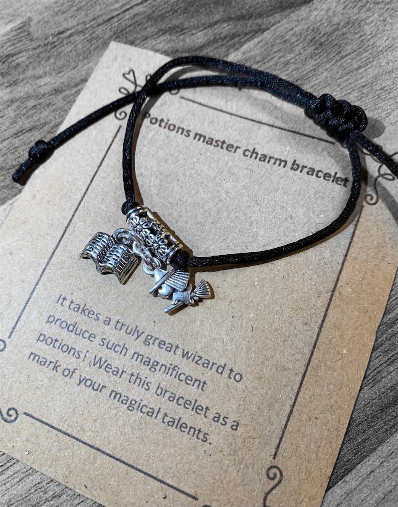 May include: Black string bracelet with silver charms, including a book, a bird, and a scroll. The bracelet is on a brown paper card with the text "Potions master charm bracelet" and "It takes a truly great wizard to produce such magnificent potions! Wear this bracelet as a mark of your magical talents."