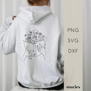 Könnte beinhalten: Ein grauer Hoodie mit einer schwarzen Linienzeichnung eines offenen Buches, aus dem Blumen herauswachsen. Das Buch wird von zwei Händen gehalten.