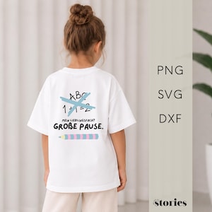 以下が含まれることがあります： 背面にグラフィックがプリントされた白い半袖Tシャツ。水色で打ち消されたABCと1+1=2の文字が特徴です。その下にはMEIN LIEBLINGSFACH? GROBE PAUSE.という文字と、ピンクと水色のストライプ柄の水平な鉛筆のグラフィックが描かれています。
