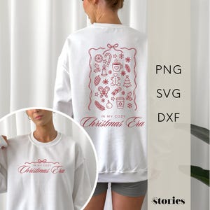 Könnte beinhalten: Weißes Sweatshirt mit einem roten Weihnachtsmotiv auf dem Rücken, das festliche Symbole wie einen Lebkuchenmann, eine Zuckerstange und einen Weihnachtsbaum zeigt. Der Text "IN MY COZY Christmas Era" ist rot gedruckt. Eine kleinere Version des Designs befindet sich auf der Vorderseite.