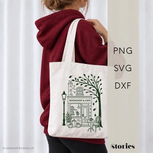 Könnte beinhalten: Eine weiße Stofftasche mit einer dunkelgrünen Grafikillustration einer Buchhandlung und eines Cafés, inklusive Baum, Laternenpfahl und Kürbissen. Der Text "BOOKSHOP & CAFE" ist auf der Fassade aufgedruckt. Die Tasche wird über einem bordeauxroten Kapuzenpullover getragen.