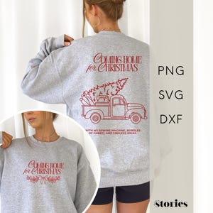 May include: A heather gray sweatshirt with the text "Coming Home for Christmas" in red script. Below the text is a red illustration of a truck carrying a Christmas tree and sewing machine. The text "WITH MY SEWING MACHINE, BUNDLES OF FABRIC, AND ENDLESS IDEAS." is below the truck.
