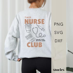 Può includere: Una felpa girocollo grigio chiaro con una grafica sul retro che riporta il testo TIRED NURSE CLUB in lettere color marrone chiaro. Il design include disegni a linee nere di un bicchiere di caffè, una siringa, uno stetoscopio, un blister di pillole e un cerotto con il testo SAVING LIVES, MISSING SLEEP.
