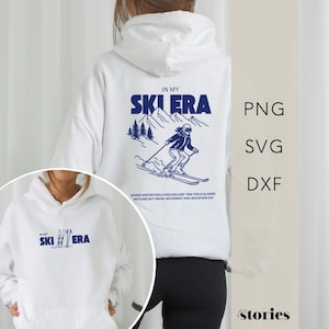 May include: White hoodie with a blue graphic on the back that says "IN MY SKI ERA" with a skier illustration. The front of the hoodie has the same text. The hoodie also has the text "WHERE WINTER FEELS ENDLESS AND TIME FEELS SLOWER, NOTHING BUT SNOW, MOVEMENT AND MOUNTAIN AIR."