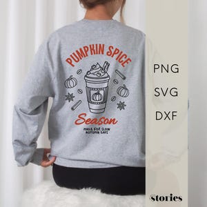 May include: A light gray crewneck sweatshirt featuring a back graphic of a coffee cup with whipped cream, pumpkins, cinnamon sticks, and star anise. The text reads PUMPKIN SPICE Season MADE FOR SLOW AUTUMN DAYS in orange and black ink.