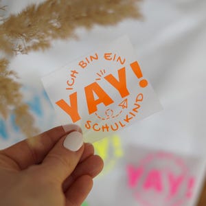 May include: Orange vinyl sticker with the text "Ich bin ein yay! Schulkind" in a circle. The sticker is on a white background.