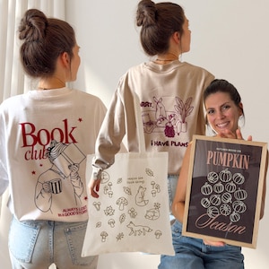 Könnte beinhalten: Ein weißes Sweatshirt mit rotem Schriftzug Book club und einer Grafik einer lesenden Person, ein beiges Sweatshirt mit kastanienbraunem Text Sorry, i have plans, eine weiße Tragetasche mit braunen Naturmotiven und ein gerahmter Druck Pumpkin Season.