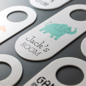 Peut inclure: Porte-nom en blanc avec un motif d'éléphant bleu clair et le texte "Jack's Room" en lettres noires.