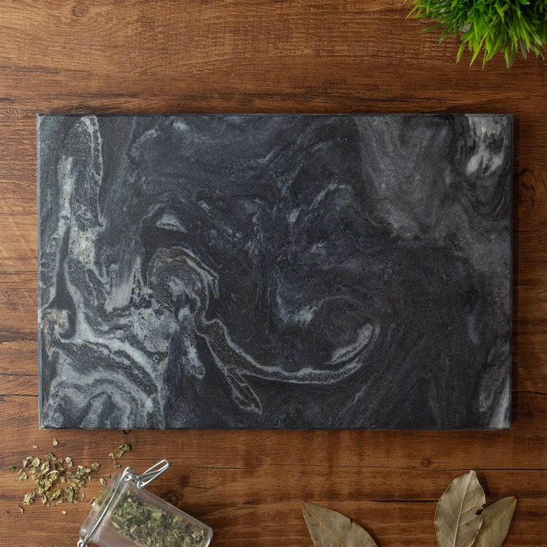 Puede incluir: Una tabla de cortar de m&aacute;rmol negro con un patr&oacute;n blanco en espiral. La tabla es rectangular y tiene una superficie lisa.
