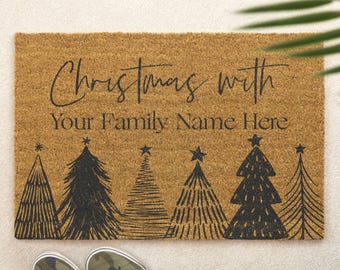 Puede incluir: Una alfombra rectangular con el texto "Christmas with Your Family Name Here" en escritura negra. Debajo del texto hay cinco diseños de árboles de Navidad negros. Zapatillas de camuflaje en la parte inferior de la imagen.