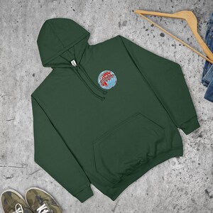 May include: A dark green hoodie with a front pocket and a drawstring hood. The sweatshirt features a circular embroidered design of a globe with red and blue accents on the upper left chest. The sweatshirt is made of a soft material.