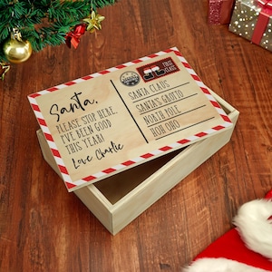 May include: A wooden box with a hinged lid, designed to resemble a letter to Santa Claus. The lid features text that reads "Santa, Please stop here. I've been good this year! Love Charlie." The box is decorated with red and white diagonal stripes.