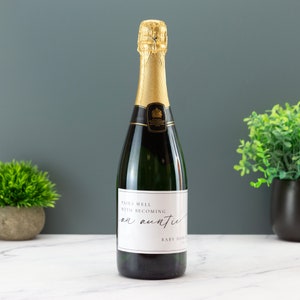 May include: A bottle of sparkling wine with a white label that says "Pairs well with becoming an auntie".