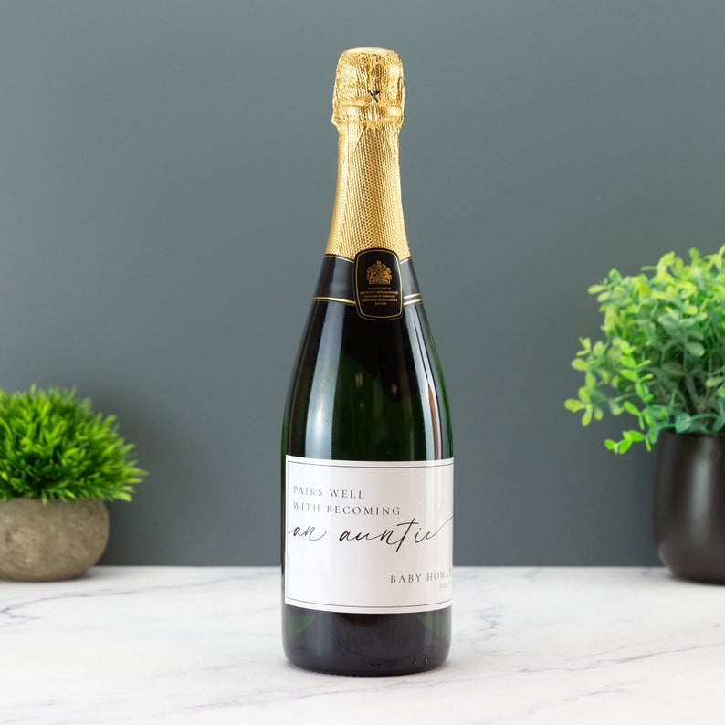May include: A bottle of sparkling wine with a white label that says "Pairs well with becoming an auntie".