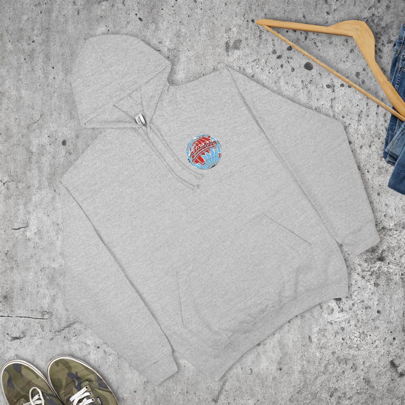 May include: A pale grey hoodie with a front pocket and a hood. The hoodie has a small, colourful emblem on the chest, showing a globe with red and blue details. The hoodie is made of a soft material and is suitable for casual wear.
