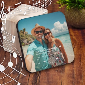 May include: Square, black-edged coaster featuring a couple on a beach, with the text "Your Custom Title Here" and "Your Custom Name(s) Here". The coaster has a music player interface design and is set on a wooden surface.