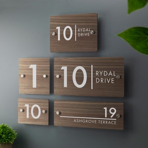 May include: Three wooden house number signs with white lettering. The top sign reads "10 Rydal Drive". The middle sign reads "1.10 Rydal Drive". The bottom sign reads "10 Ashgrove Terrace 19."