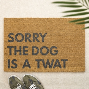 May include: A brown doormat with the text "SORRY THE DOG IS A TWAT" in black lettering.