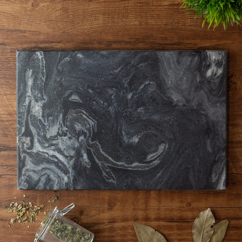 May include: A black marble cutting board with a swirling white pattern. The board is rectangular and has a smooth surface.