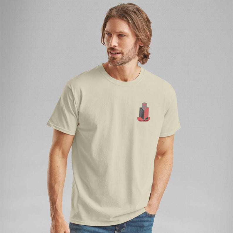 K&ouml;nnte beinhalten: Cremefarbenes T-Shirt mit einem kleinen, stilisierten Geb&auml;ude-Grafik in Rot, Schwarz und Grau. Die Grafik befindet sich auf der linken Brust. Das Shirt hat einen Rundhalsausschnitt und kurze &Auml;rmel.