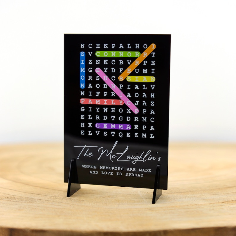 May include: Black acrylic sign with a word search puzzle featuring the words "The McLaughlin's", "Family", "Connor", "Simon", "Gemma", and "Nice". The sign has a white stand and the text "Where memories are made and love is spread" is printed below the puzzle.