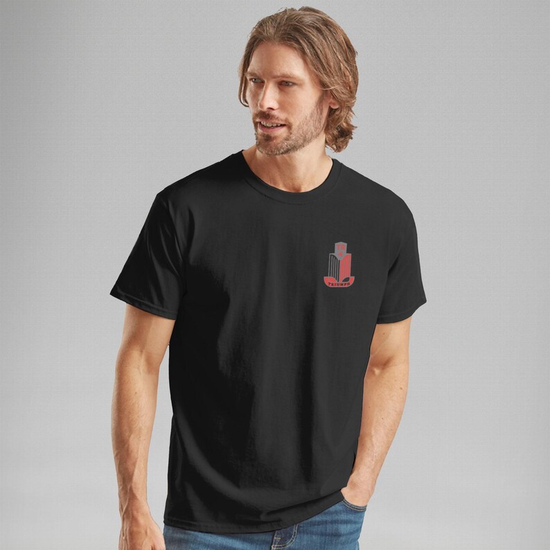 K&ouml;nnte beinhalten: Schwarzes T-Shirt mit Rundhalsausschnitt und einem kleinen roten und grauen Geb&auml;ude-Design auf der linken Brust. Das Wort "Valhalla" ist darunter in Rot gedruckt. Das Shirt ist aus weichem Material.