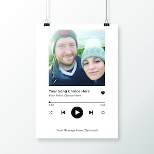 May include: A digital music player interface with a photo of a couple in winter clothing. The text "Your Song Choice Here" and "Your Artist Choice Here" is displayed. The music player controls include a play button, a rewind button, a fast forward button, and a repeat button.