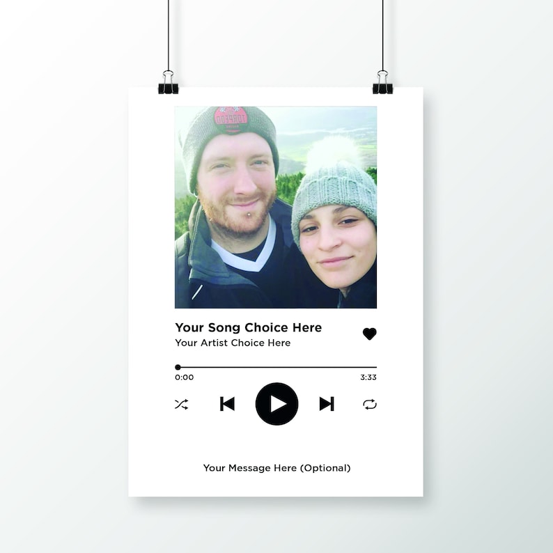 May include: A digital music player interface with a photo of a couple in winter clothing. The text "Your Song Choice Here" and "Your Artist Choice Here" is displayed. The music player controls include a play button, a rewind button, a fast forward button, and a repeat button.