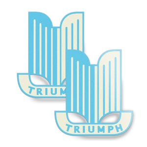 May include: Two light blue and cream Triumph logo stickers. The stickers feature a stylized design with vertical stripes and the word "TRIUMPH" in a curved banner at the bottom. The stickers are on a white background.