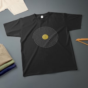 May include: A black short-sleeve t-shirt featuring a graphic of a vinyl record in the center. The record has white text spiraling around a yellow circular label in the middle that reads YOUR ARTIST HERE.