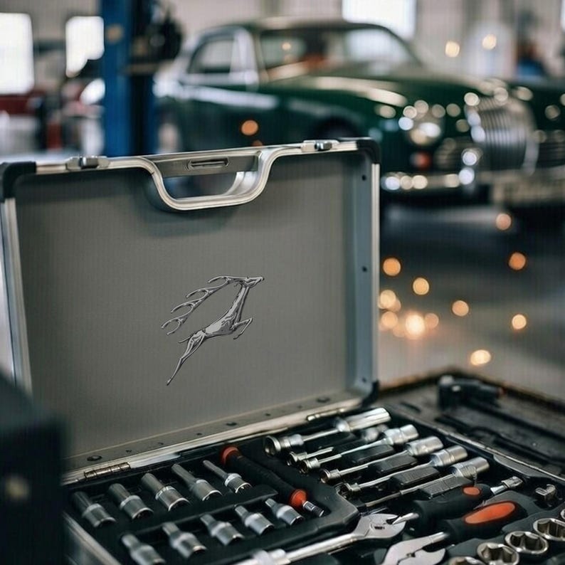 May include: A gray metal toolbox with a silver deer emblem, open to reveal a set of tools. The tools include sockets, wrenches, and screwdrivers. A classic green car is in the background.
