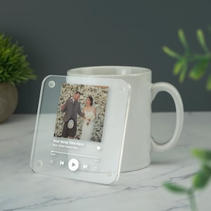 以下が含まれることがあります： 写真と音楽プレーヤーインターフェースが描かれた透明なアクリルコースター。音楽プレーヤーのテキストには「Your Song Title Here」と「Your Artist Name Here」と表示されています。