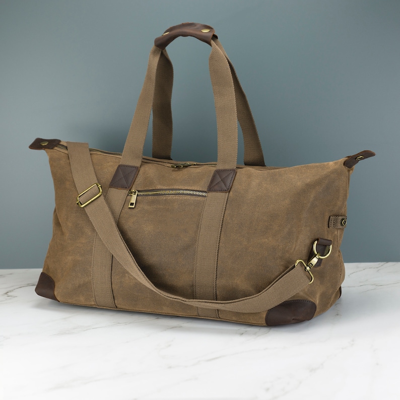 May include: A brown canvas duffel bag with leather accents and a zipped pocket. The bag has a top handle and a detachable shoulder strap.