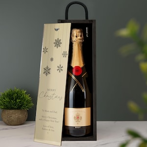 May include: A dark wooden wine box with a black handle containing a champagne bottle. The sliding lid is gold with black snowflake graphics and text that reads: Merry Christmas, To Mum and Dad, Merry Christmas, and a Happy New Year! Lots of love, Robert & Lisa x.
