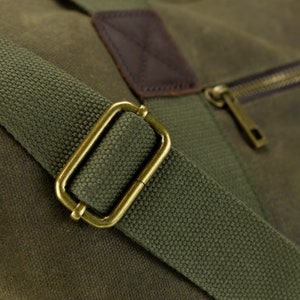 May include: Close-up of a green canvas duffel bag with a brown leather patch and a brass buckle on the strap.
