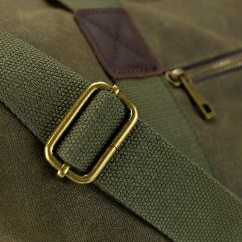 May include: Close-up of a green canvas duffel bag with a brown leather patch and a brass buckle on the strap.