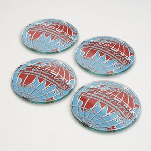 May include: Four round glass coasters with a globe design. The globe features a red landmass, blue oceans, and a silver outline. The word "Academy" is written across the globe in silver. The coasters are on a white background.