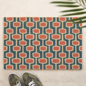 May include: A rectangular doormat featuring a repeating geometric pattern of rounded coral-coloured rectangles connected by dark teal vertical lines. The mat has a textured, natural fibre surface and is positioned on a light-coloured floor.