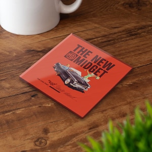 Puede incluir: Posavasos cuadrado con fondo rojo, con una ilustración de coche vintage y el texto "THE NEW MIDGET". El posavasos también incluye el texto "THE CAR THAT... Sports ahead". Una taza blanca está en el fondo.