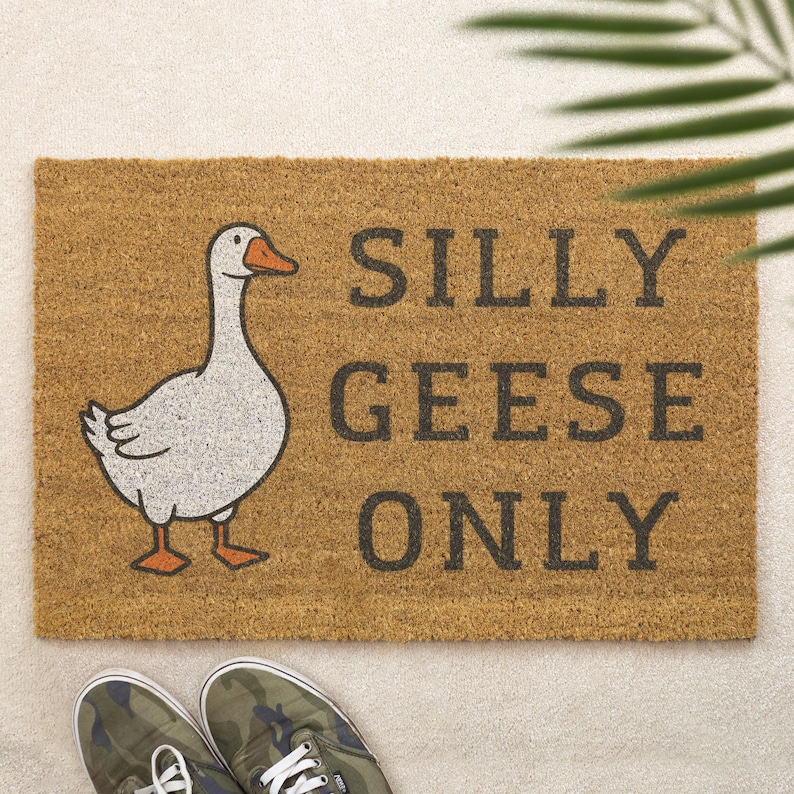 May include: A rectangular doormat made of brown coir fiber. It features a cartoon goose illustration and the text "SILLY GEESE ONLY" in dark gray letters. Camouflage sneakers are visible at the bottom.