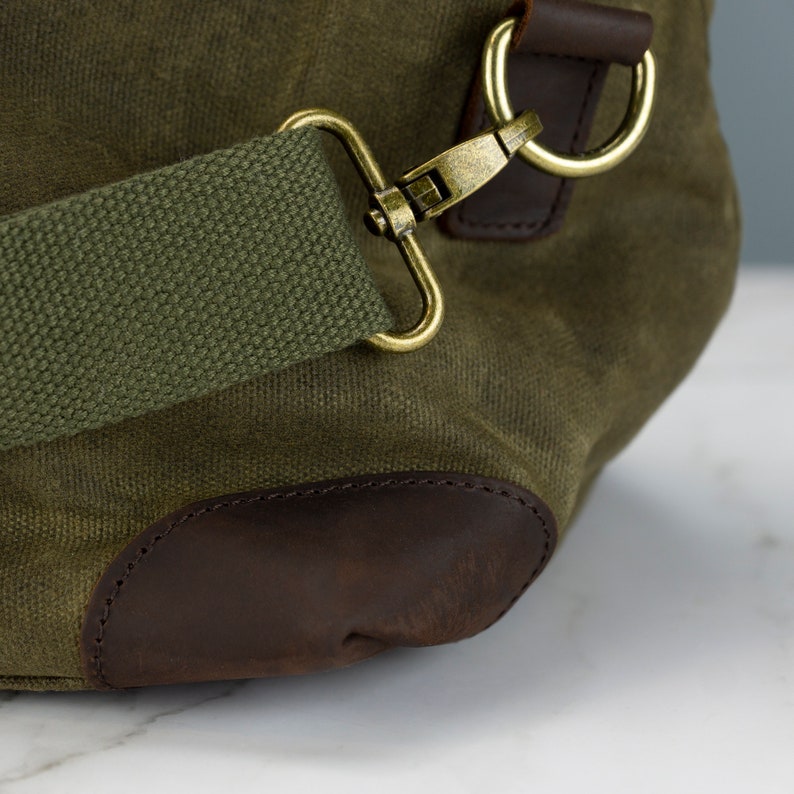 May include: A green canvas duffel bag with brown leather accents and a brass clasp. The bag has a shoulder strap and a top handle.