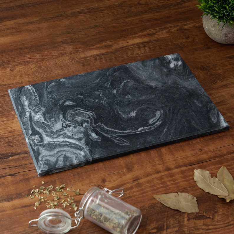 Puede incluir: Una tabla de servir de m&aacute;rmol negro con patrones blancos en espiral. La tabla est&aacute; sobre una superficie de madera.