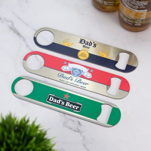 Könnte beinhalten: Drei Flaschenöffner aus Metall mit silberner Oberfläche. Jeder Öffner hat ein anderes Design mit dem Text "Dad's Beer" und einem anderen Hintergrund: blau, rot und grün.