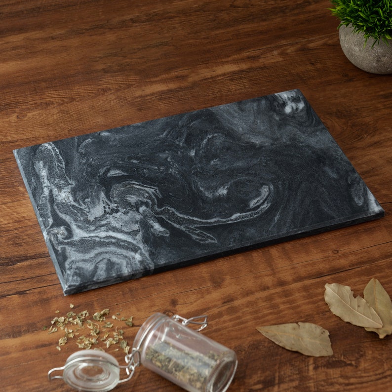 May include: A black marble serving board with white swirling patterns. The board is on a wooden surface.